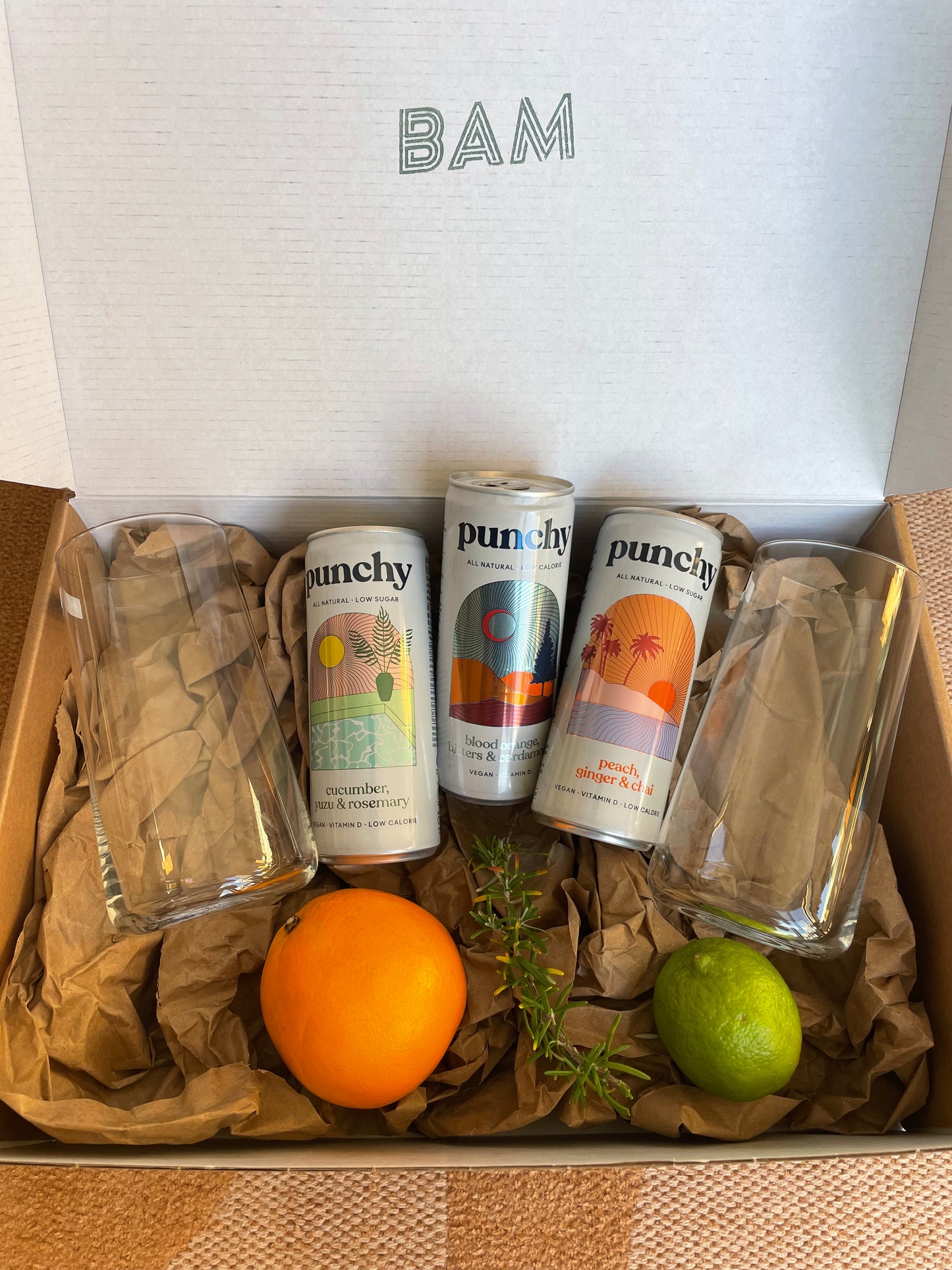 Coffret mocktails sans alcool avec canettes, verres et garnitures fraîches, idéal pour un cadeau chic et original.
