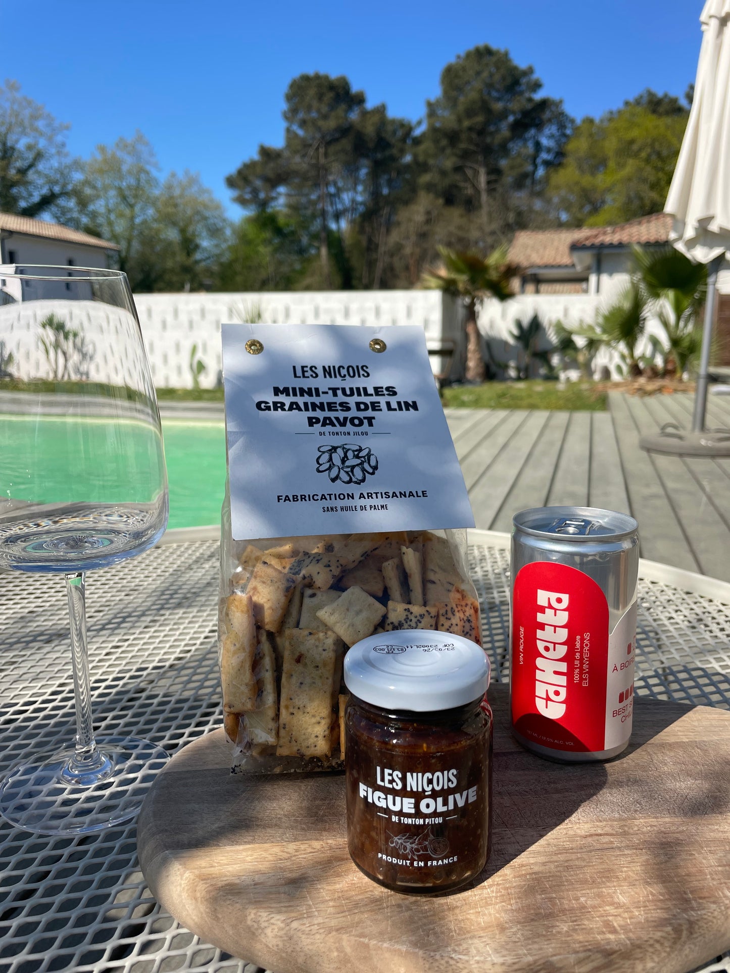 Pack apéro Red Crush de Maison BAM – vin rouge en canette, tartinade figues & olives, tuiles aux graines de lin, sur fond d’été ensoleillé avec vue sur les pins