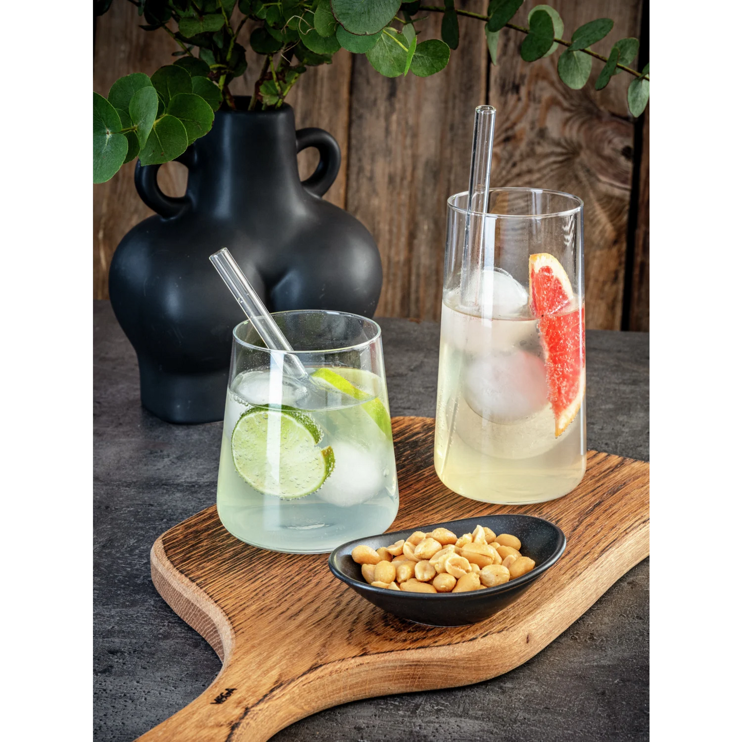 jolis verres remplis de boissons, agrumes, et glaçons sur une planche en bois, bol de cacahuètes et vase avec eucalyptus