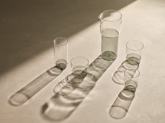 verres à cocktails ou mocktails et carafe gris transparent, sur béton ciré, lumière mettant en evidence l'ombre de la verrerie