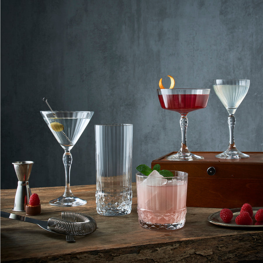 verres à cocktail garnis disposés sur une table élégante, passoire et doseur à cocktails, framboise servies sur une petite assiette
