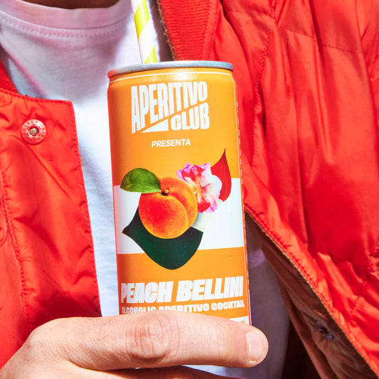 homme vêtu d'un tee shirt blanc et bombers rouge tenant une canette de pêche bellini avec paille à rayures jaunes