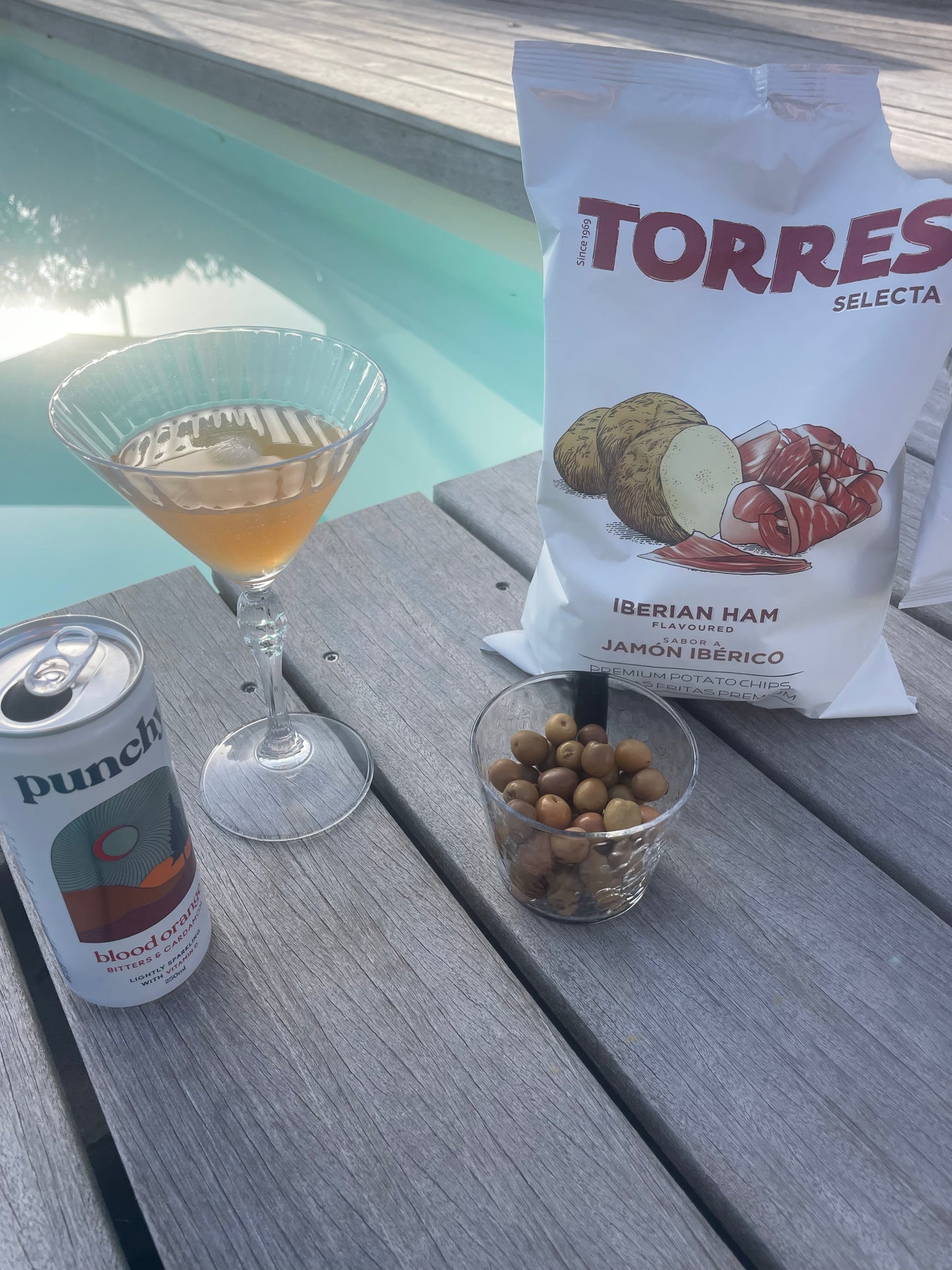 chips torres au jambon ibérique, olives dans un ramequin, mocktail servi dans un verre à pied elegant au bord de la piscine