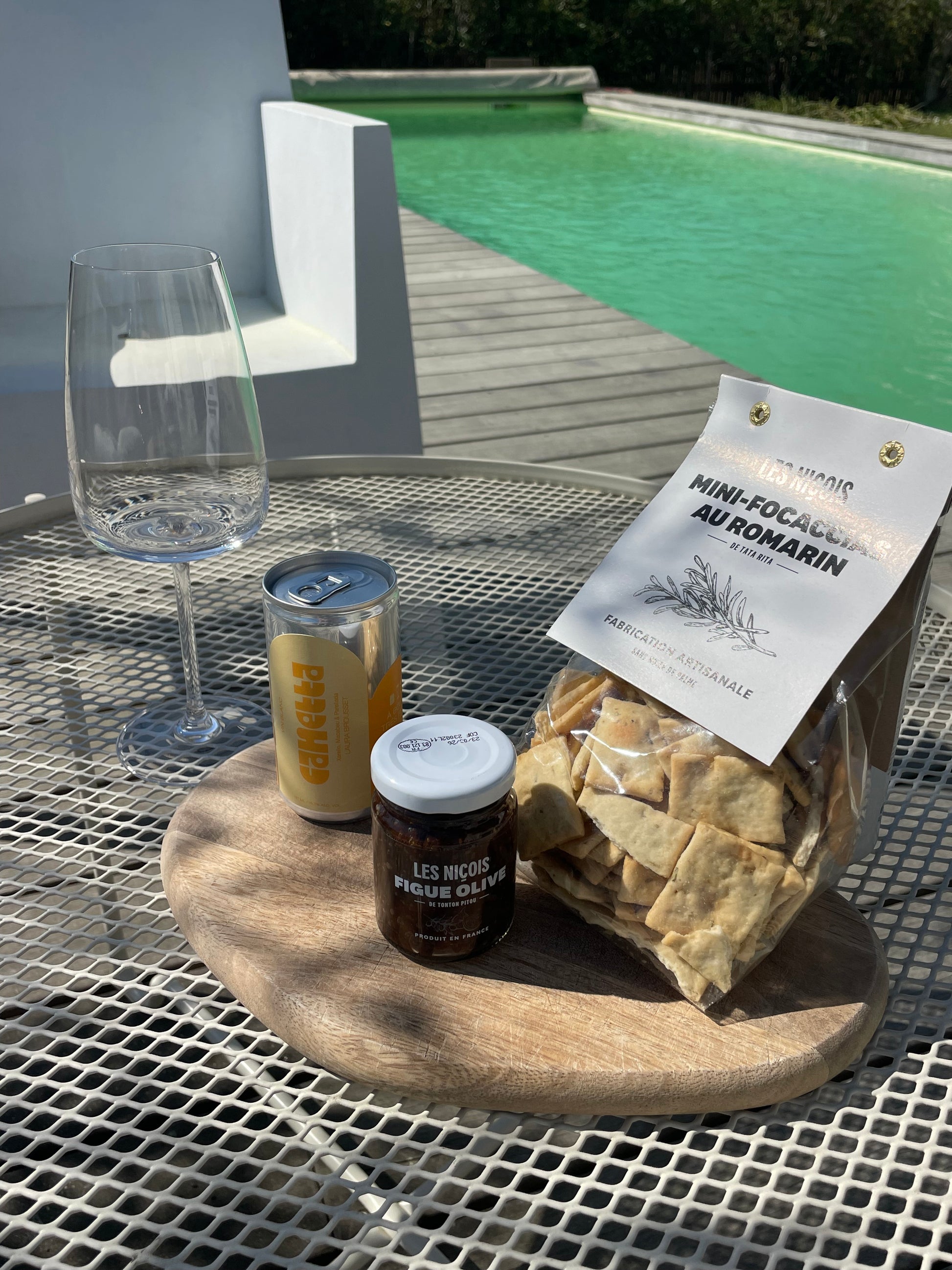 le pack vin blanc, mini foccacia, tartinade figue olive avec un verre à pied  sur une table basse au bord de la piscine, prêt à déguster