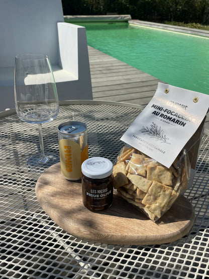 le pack vin blanc, mini foccacia, tartinade figue olive avec un verre à pied  sur une table basse au bord de la piscine, prêt à déguster