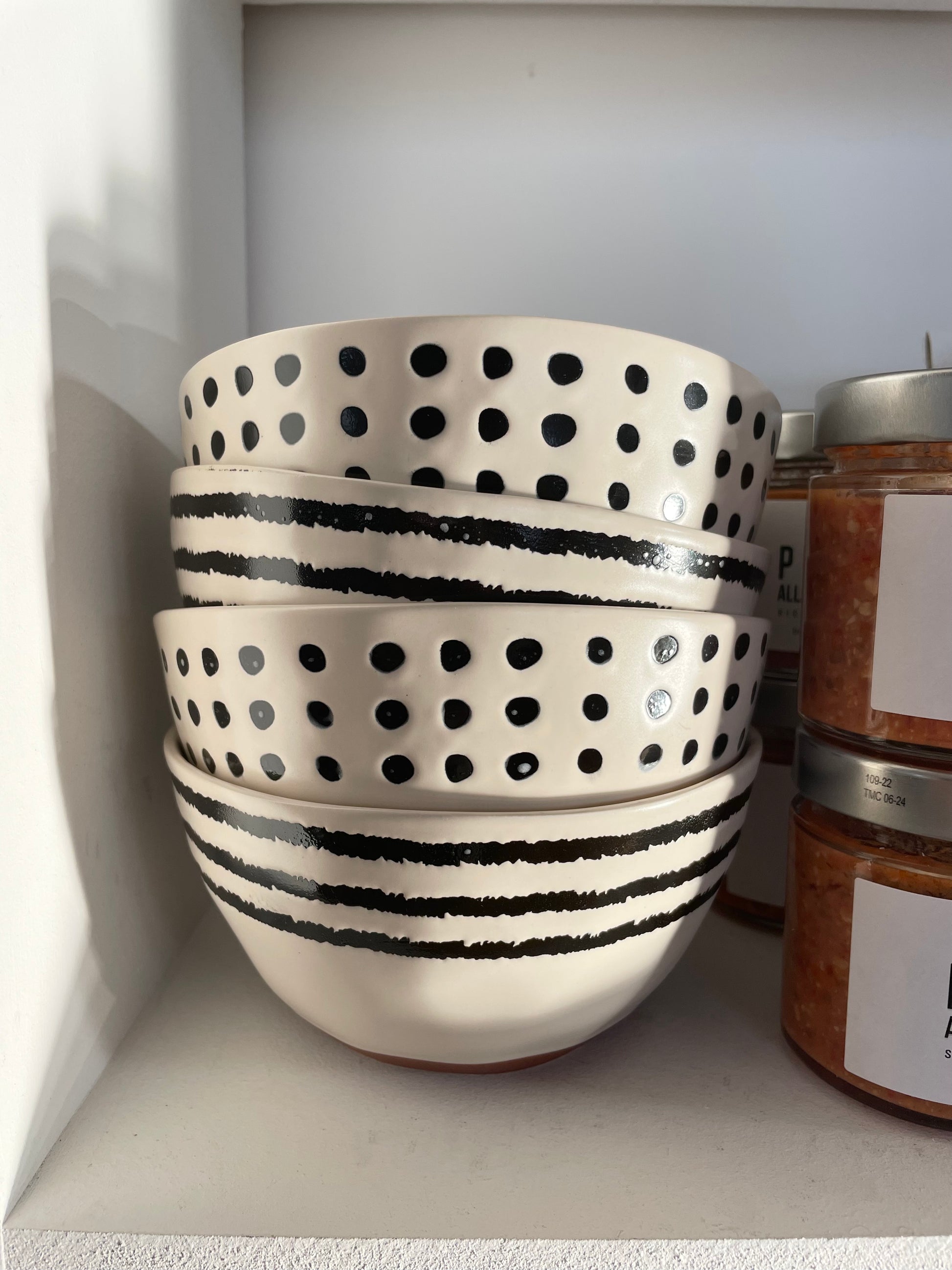 bols empilés dans une étagère, rayures noires ou pois noirs peints à la main. 