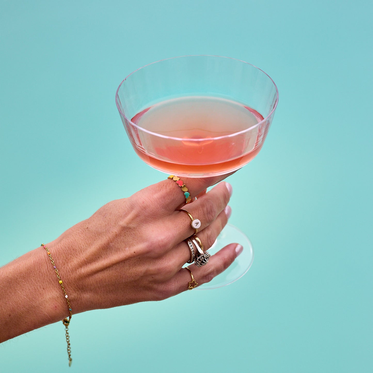 main de femme avec bagues tenant verre à pied rempli de cosmopolitan au dessus de la piscine