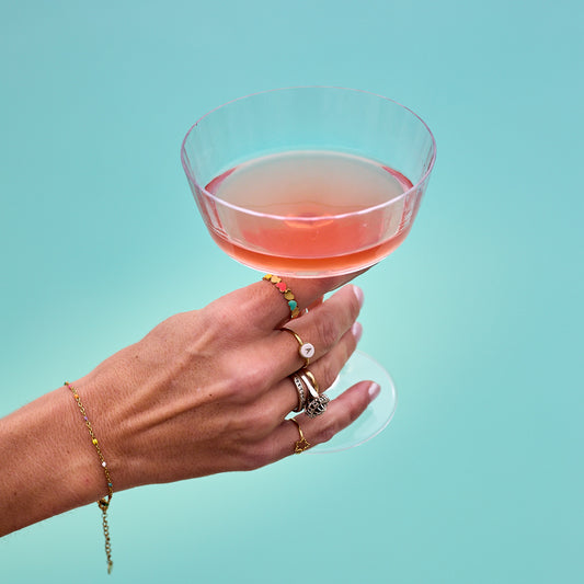 main de femme avec bagues tenant verre à pied rempli de cosmopolitan au dessus de la piscine