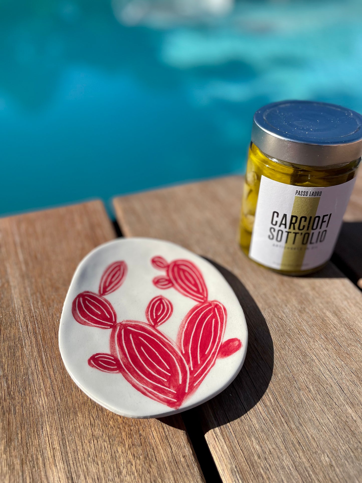 coupelle artisanale en céramique, cactus rouge sur fond blanc, avec un bocal d'artichauts à l'huile d'olive, en terrasse