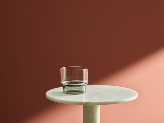 verre gris transparent forme graphique, posé sur une table en marbre blanc, mur de couleur terracotta