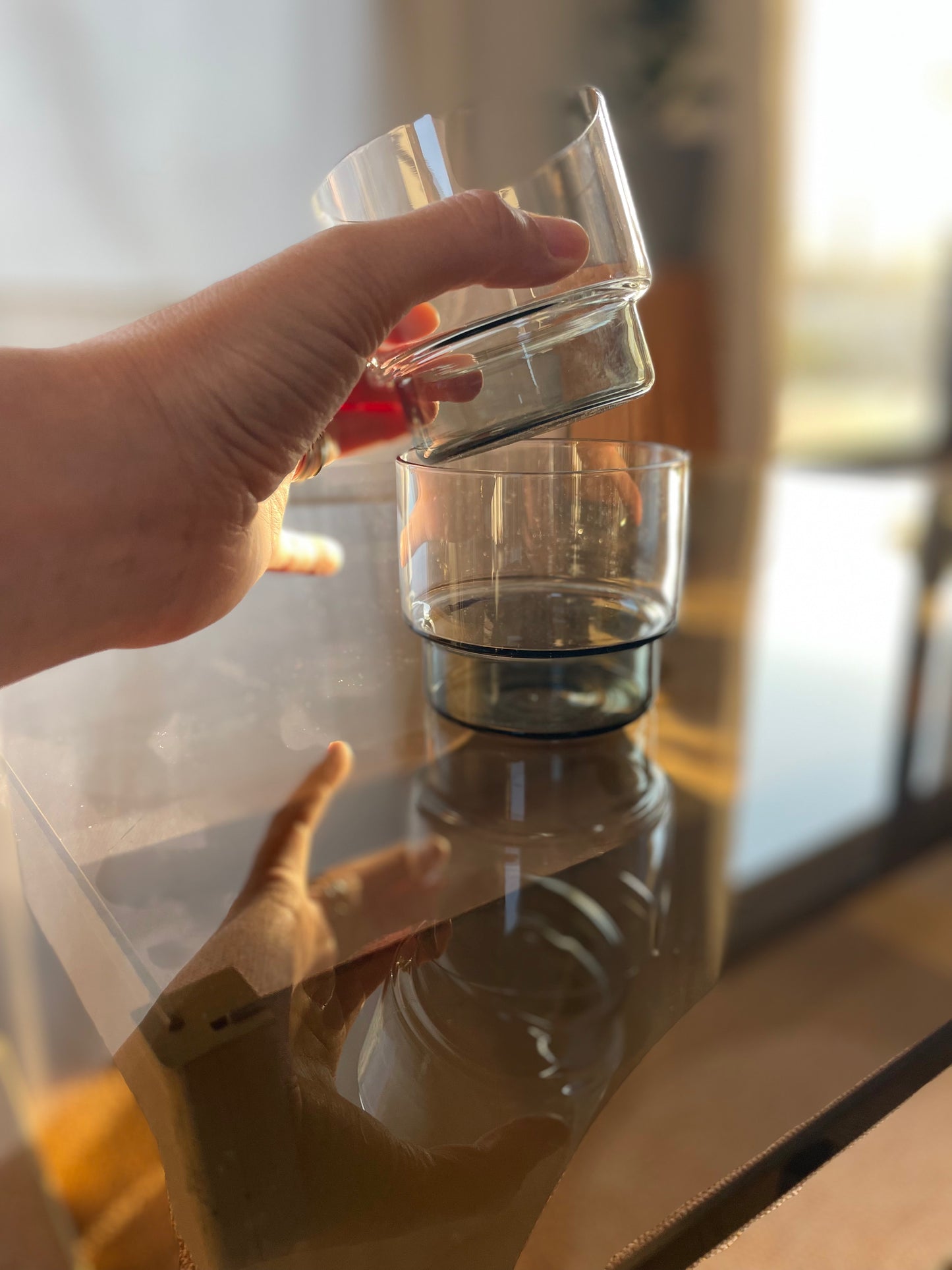 main qui empile 2 verres bas transparent fumé sur une table en verre