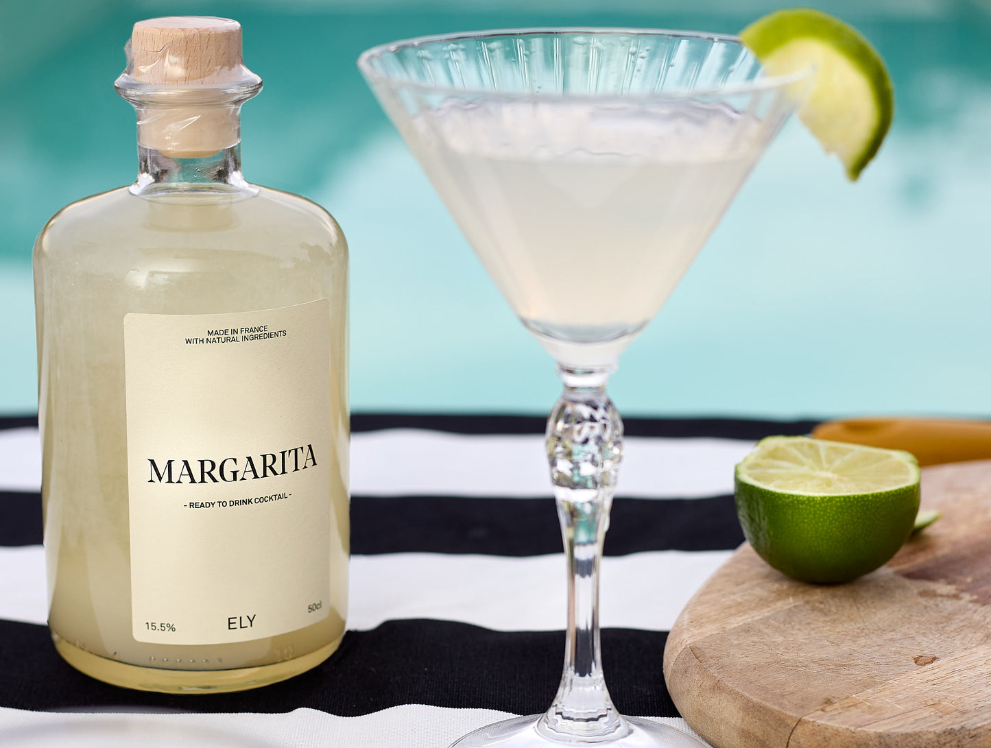 margarita en bouteille posé sur une table au bord de la piscine avec verre à martini et rondelle de citron vert rempli ddu cocktail