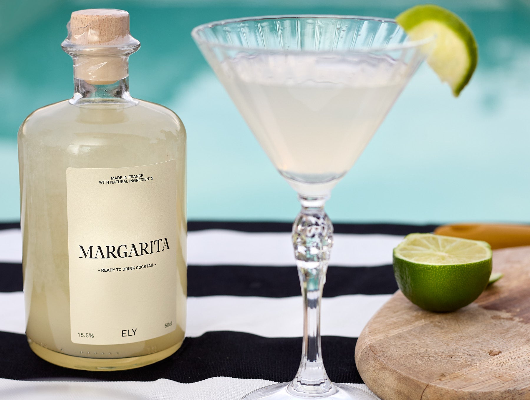 margarita en bouteille posé sur une table au bord de la piscine avec verre à martini et rondelle de citron vert rempli ddu cocktail