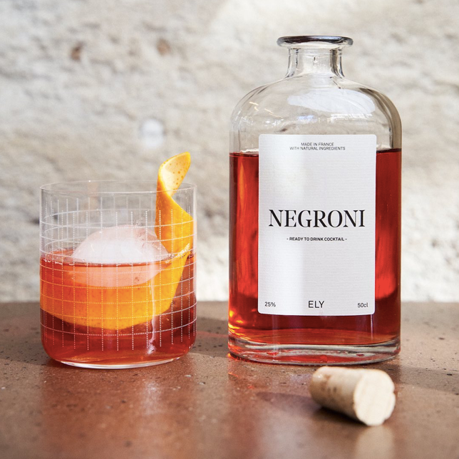 verre à cocktail garni de negroni tout prêt avec gros glaçon et écorce d'orange. bouteille de negroni ouverte