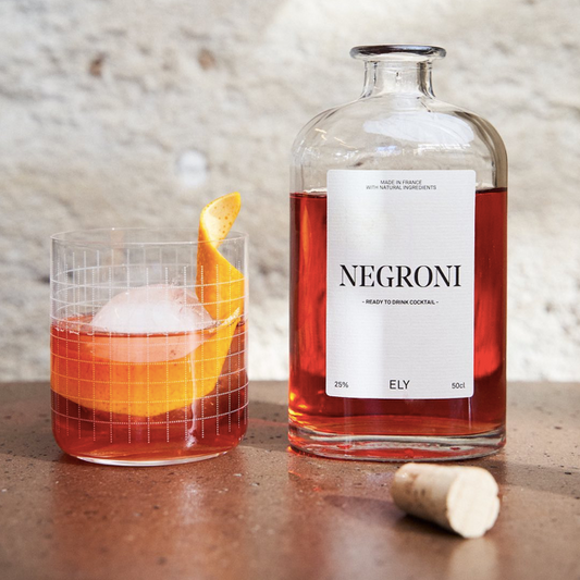 verre à cocktail garni de negroni tout prêt avec gros glaçon et écorce d'orange. bouteille de negroni ouverte