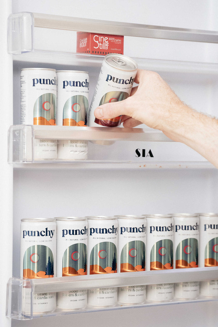 dix canettes de punchy orange sanguine dans une porte de frigo, une main d'homme en prend une dans l'étagère