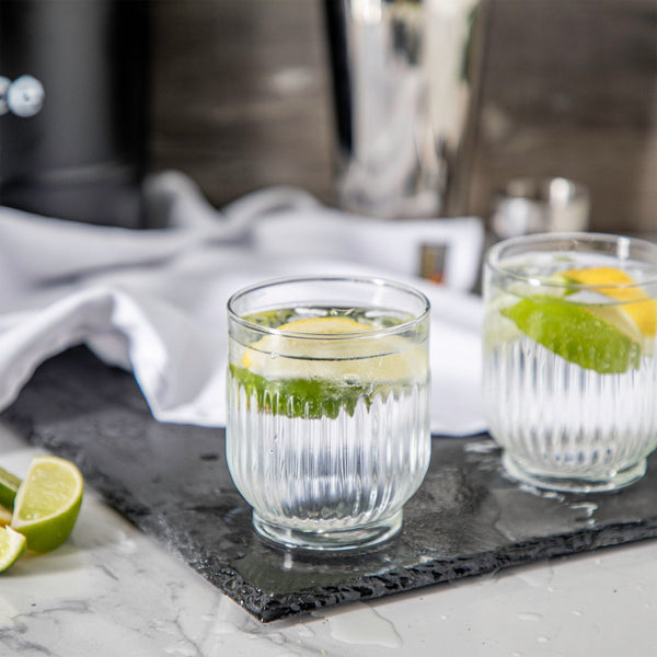verres ciselés vintage, posé sur un plan de travail, remplis d'eau et de quartiers de citrons et cittons verts, 