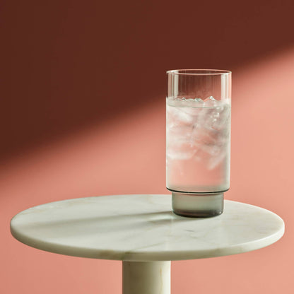 verre highball, haut et étroit, rempli d'eau et de glaçons posé sur une table en marbre 